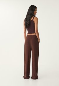 Bruna vida byxor och en figurnära mörk ärmlös topp, båda gjorda av mjukt material, med hög midja och sidofickor.