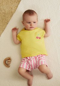 T-shirt en coton jaune avec une poche ornée d'une broderie de cerise, accompagnée d'un short rayé rose et blanc, sur une couverture crème texturée.