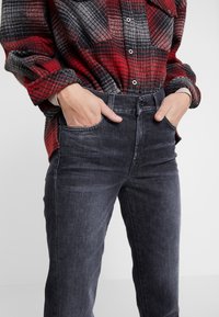 Jeans de mezclilla negros con un corte ajustado, que cuentan con bolsillos delanteros y una cintura de altura media. La tela tiene una textura ligeramente desgastada.