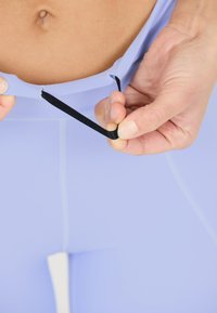 Ljuslila idrottstopp med ett svart band som dras; har en slät, elastisk textur och en figurnära design.