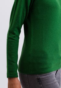 Zielony sweter dzianinowy z długimi rękawami, teksturowana tkanina, dopasowany fason i okrągły dekolt. Wykończone mankiety i dół z delikatnymi bocznymi rozporkami.