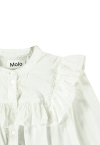 Blusa bianca con colletto arricciato, dotata di chiusura a pulsante sul davanti. Realizzata in un tessuto leggero con una texture liscia.
