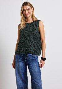Zelený bezrukávový top s černým leopardím vzorem, lehká látka, kulatý výstřih a volný střih, doplněný modrými širokými jeansy.