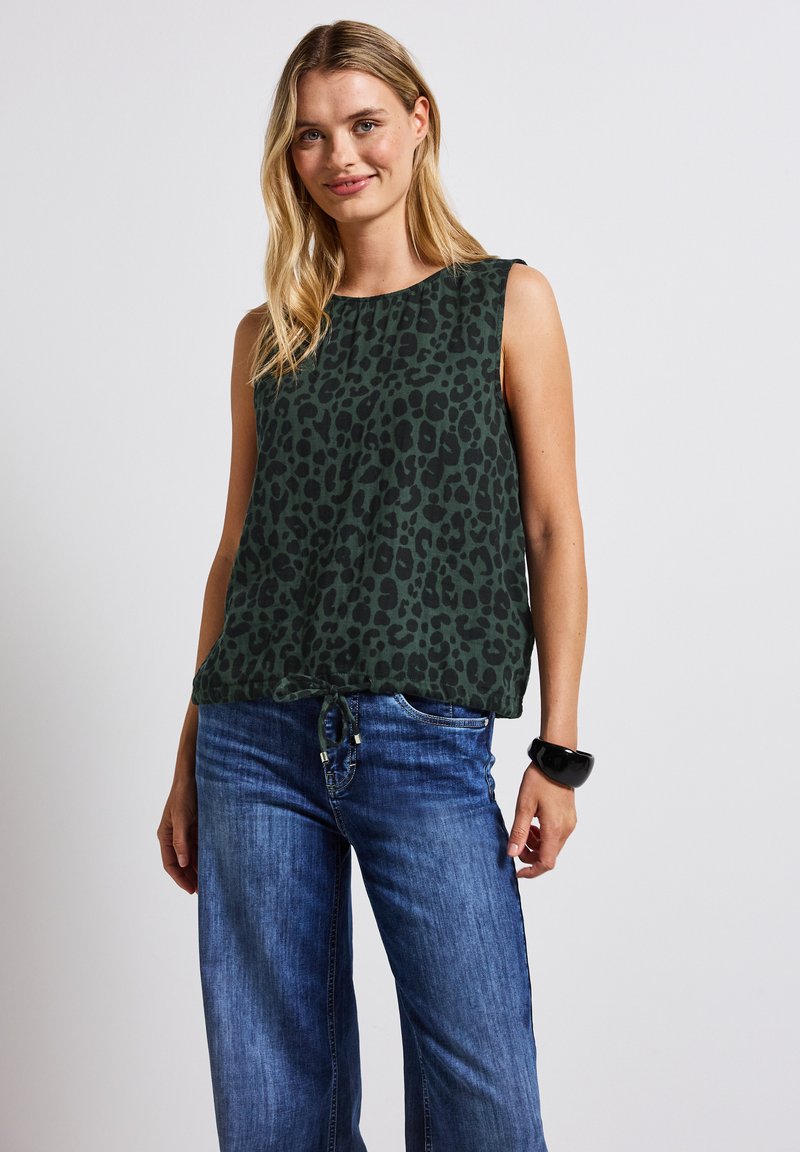 Zelený bezrukávový top s černým leopardím vzorem, lehká látka, kulatý výstřih a volný střih, doplněný modrými širokými jeansy.
