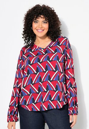 Blouse à manches longues présentant un motif géométrique en rouge, bleu, blanc et noir, avec un décolleté en V et des poignets froncés. Texture de tissu lisse.