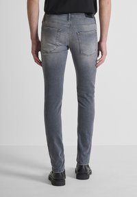 Jeans in denim grigio con taglio slim, dotati di due tasche posteriori e una texture liscia, abbinati a scarpe nere.