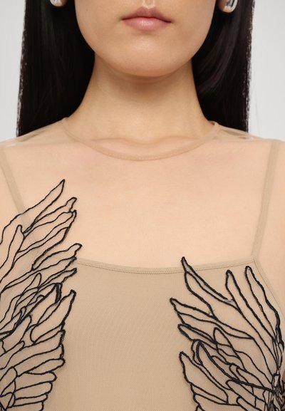 Top beige trasparente con intricati motivi di foglie ricamati in nero sul petto, caratterizzato da un colletto rotondo e spalline sottili.