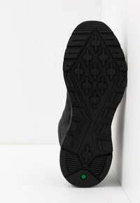Schwarze Bootsohle aus strukturiertem Gummi, mit einem Profilmuster aus Kreuzen und Sechsecken, versehen mit dem Schriftzug 'Timberland' und einem grünen Akzent.