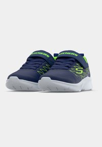 Jūras zila un neona zaļa Skechers bērnu sporta apavi ar baltām zolēm un velcro siksnām, parādīti no priekšpuses uz baltā fona.