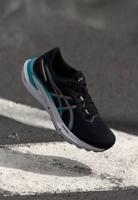 Zwarte sportieve schoen met een ademende mesh bovenkant,accenten in teal en oranje, met een gevoerde zool en getextureerde details.
