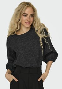 Blusa nera texturizzata con scollatura rotonda, maniche a sbuffo e vestibilità morbida. Abbinata a pantaloni neri a vita alta.