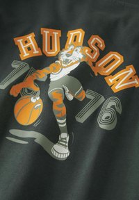 Maglietta grafica verde scuro con un cartone animato di una tigre in maglia da basket, che tiene in mano un pallone da basket arancione, con "HUDSON 76" in bold arancione.