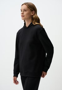 Czarna bluza z kapturem wykonana z miękkiego, teksturowanego materiału. Charakteryzuje się luźnym krojem, długimi rękawami i prostym designem bez widocznych logo czy wzorów.