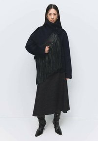 Abrigo de lana azul marino de gran tamaño con cuello alto, combinado con una falda gris oscuro y un bolso de mano negro con flecos. Botas negras altas hasta la rodilla y de punta afilada.