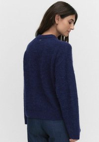 Granatowy, teksturowany sweter z dzianiny z okrągłym dekoltem i opadającymi ramionami. Posiada mały detal z guzikami z tyłu.