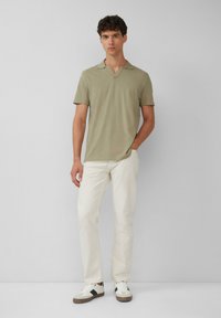 Olijfgroene polo met korte mouwen en een V-hals, gecombineerd met lichtbeige broeken en witte sneakers. Eenvoudig ontwerp, zachte textuur.