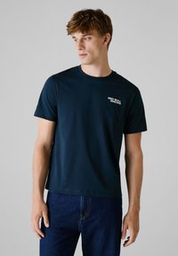 Donkerblauwe t-shirt met korte mouwen van een gladde stof, voorzien van een klein wit logo op de linkerkant van de borst. Casual pasvorm met een ronde hals.