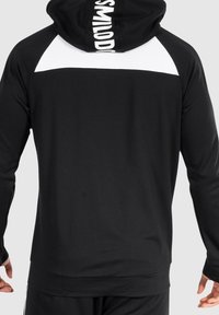 Sudadera negra con paneles blancos en los hombros, que presenta un logo destacado en la parte trasera. Tejido suave y texturizado con un diseño ajustado y mangas largas.