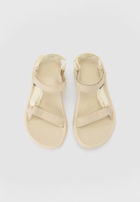 Beige sandaler med justerbare stoffremmer, polstret fotseng og gummisåle. Glatt tekstur, formet design for komfort.