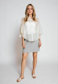 Sheer cream blouse with oversized sleeves, paired with a light gray skirt featuring pockets and a relaxed fit. Light beige sandals complete the look.