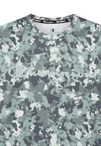 Camisa de manga corta en un patrón de camuflaje gris-azul, con un logo de Champion blanco, cuello redondo y textura de tela suave.