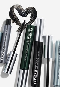Quatre tubes de mascara de couleurs différentes : argent, vert, noir et bleu. Chacun présente un étiquetage et des bouchons distincts, avec une trace de mascara noir.