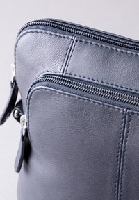 Gray leather bag featuring two zippers, textured finish, and contrasting stitching along the edges for added detail.
