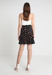 Svart kjol med blommönster och vita prickar, med volangkant och resårmidja. Kombinerad med en vit camisole.