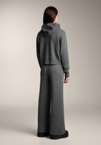 Strihaná sivá pletená mikina s kapucňou, doplnená voľnými sivými širokými nohavicami. Hladká textúra, minimálne detaily a bočné švové prešívanie.