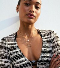 Svart och vit randig stickad cardigan, lager av guldkedjor med en pärla och stänger pendant, närbild på en texturerad yta och halsringning.