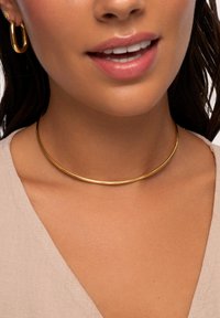Goldfarbener Metall-Choker-Halsreifen mit einem eleganten, glatten, runden Design, der auf einem nackten Schlüsselbein ruht, kombiniert mit passenden Creolen.