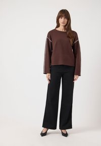 Pull marron à manches larges avec un biais blanc le long des coutures, accompagné d'un pantalon noir à jambes larges et de ballerines noires.