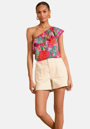 Ein einseitiger, pinkfarbener Blumenoberteil mit Rüschen und Pompon-Akzenten, kombiniert mit beigen Shorts, die über Fronttaschen und ein strukturiertes Design verfügen.