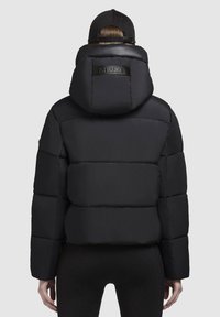 Svart puffjacka med huva, med ett fyrkantigt quiltat mönster och en logotyp på baksidan. Slät textur och kortare längd.
