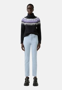 Černý pletený svetr s vzorovaným fialovým a bílým žebrovaním, v kombinaci se světle modrými kalhotami a robustními černými platformovými botami.