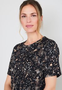 Zwarte top met korte mouwen, voorzien van een gemengd dierenprint in beige en witte tinten. Ronde halslijn en zachte textuur.