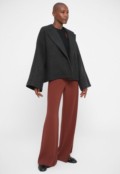 Chaqueta oversized de lana gris con mangas anchas, combinada con pantalones de pierna ancha color óxido. Tela suave y corte ajustado. Zapatos negros completan el look.