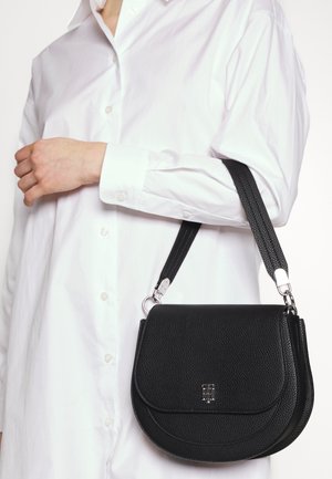 Černá kožená krosbody taška s kulatým klopovým designem, texturovaným povrchem, stříbrným kováním a nastavitelným popruhem.