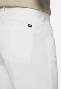 Vita bomullsbukser med en slät yta, med en bakficka och en liten blå logodetalj. Skräddarsydd passform med diskreta sömdetaljer.