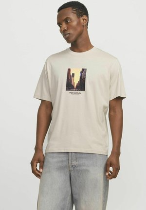 Beige katoenen t-shirt met een kleine urban grafiek op de voorkant, korte mouwen en een losse pasvorm, gecombineerd met lichtblauwe denim shorts.