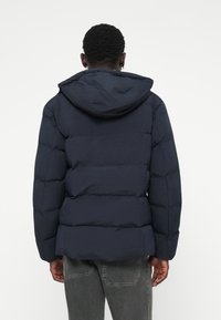 Marineblaue Steppjacke mit Kapuze, mit gesteppten Abschnitten und elastischen Bündchen. Glatte Textur und lässige Passform.