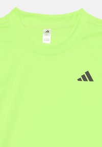Foszforeszkáló zöld sportpóló, könnyű anyagból készült, kerek nyakkal és fekete Adidas logóval a mellkason.