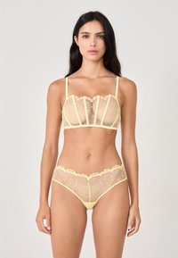 Geel mesh lingerie set met bloemembroidery, kantafwerking en een onderstructuur. De beha heeft gestructureerde panelen en de slips hebben bijpassende details.