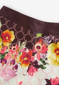 Tāls plāns ar audumu, uz kura ir dzīvīgu daudzkrāsainu ziedu raksts uz balta un tumši brūna šūnu raksta, ar tumši brūnu vidukļa joslu.