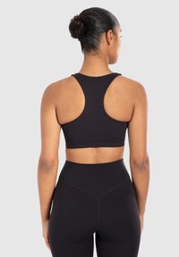 Zwarte sport-bh met een racerback ontwerp. De stof lijkt glad, aansluitend en naadloos. Draag het met bijpassende high-waisted legging.