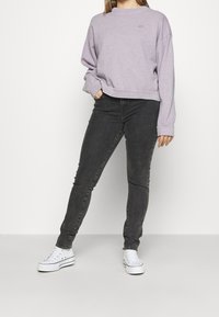 Sudadera lila claro con cuello redondo y hombros caídos, combinada con jeans ajustados gris oscuro y zapatillas blancas.