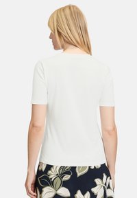 Witte aansluitende t-shirt met korte mouwen, ronde halslijn, zachte textuur en een eenvoudige achterkant. Gecombineerd met een rokje met bloemenpatroon.