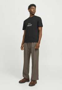 Sort bomulds t-shirt med bjerggrafik, parret med løst siddende grå bukser og brune snørebåndssko. Enkel, moderne design.