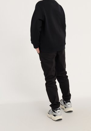 Czarna bluza z okrągłym dekoltem, zestawiona z czarnymi, zwężanymi spodniami oraz szarymi sneakersami z czarnymi i białymi akcentami.