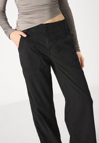 Black wide-leg pants made of cotton fabric featuring two front pockets, visible stitching, and double-button closure at the waistband.